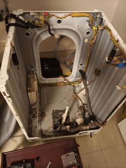 Wnętrze częściowo rozebranej pralko-suszarki, widoczna pompa oraz podłączenia elektryczne i hydrauliczne.