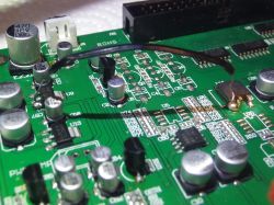 Nahaufnahme einer Leiterplatte mit sichtbaren elektronischen Bauteilen und einem dünnen Draht, der auf ihrer Oberfläche verlötet ist.