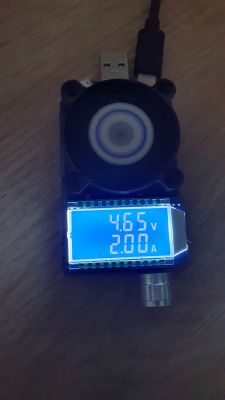 Tester USB z wentylatorem pokazuje 4,65 V i 2,00 A na tle drewnianego blatu