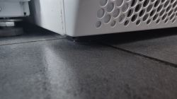 Zbliżenie na dolny róg białej suszarki na ciemnej podłodze z widoczną wodą pod urządzeniem.