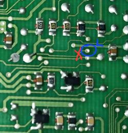 Zbliżenie PCB z elementami SMD i ścieżkami; czerwony X i niebieskie kółko wskazują punkt na płytce
