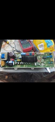 Płytka elektroniczna z różnymi komponentami i multimetrem na stole.