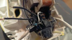 Zbliżenie na wnętrze urządzenia elektrycznego z widocznymi czarnymi i białym przewodem podłączonymi do kostki oraz rezystorem.