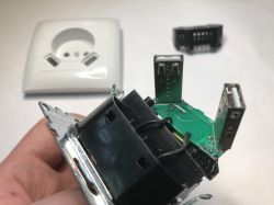 Disassembled power outlet module with a green PCB and two USB-A ports, held in a hand.
