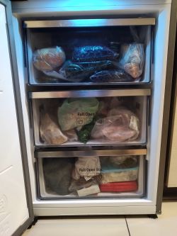 Widok wnętrza zamrażarki z trzema szufladami pełnymi zamrożonych produktów.