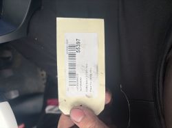 A hand holds a label with a barcode and the number 55397 against a car interior background.
