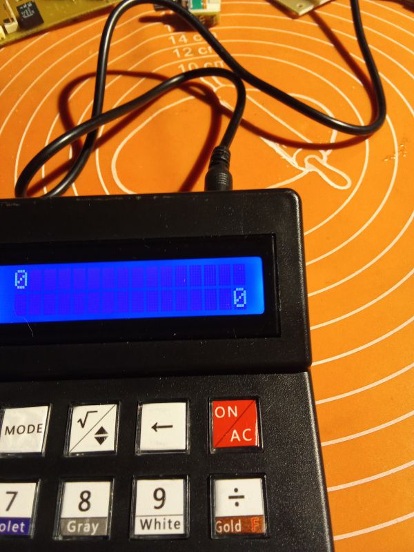 Kalkulator z niebieskim wyświetlaczem podłączony do zasilania.