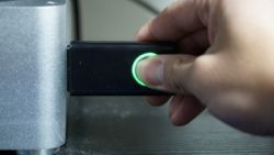 Person inserting a black USB flash drive with a fingerprint sensor into a computer.