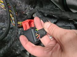 Close-up of a hand holding an automotive wiring harness and a plastic electrical connector with colored wires.