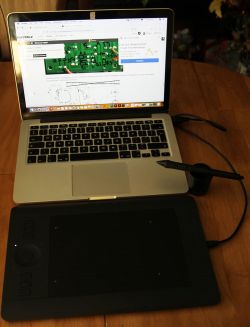 Laptop i tablet graficzny na drewnianym stole z wyświetlonym schematem.