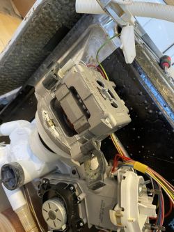 Zbliżenie na wnętrze zmywarki Bosch, widoczne dwa silniki z przewodami i plastikowymi elementami hydraulicznymi.