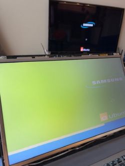 Laptop Samsung z problemem z wyświetlaniem obrazu na matrycy, obok telewizor z poprawnym obrazem.