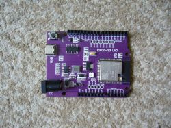 A purple ESP32-S3 UNO electronic board with connectors and components, lying on a beige carpet.