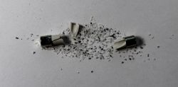 Shattered fuse with scattered glass material on a white background.
