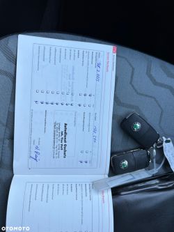 The image shows a service booklet with filled-in service entries, lying on a car seat. Two Škoda car keys are visible beside it.