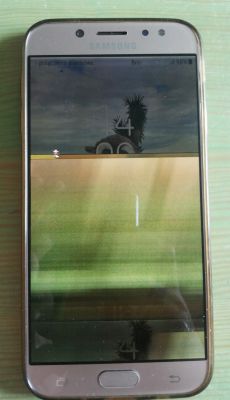 Smartfon Samsung Galaxy J7 2017 z uszkodzonym wyświetlaczem, na którym widać zniekształcenia obrazu i jasny punkt.