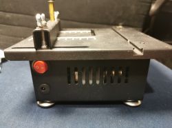 Czarny sprzęt elektroniczny z widocznym czerwonym przyciskiem zasilania i metalowymi elementami u góry na tle ciemnym.