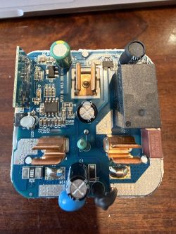 PCB of a smart switch with relay, capacitors and an edge-mounted module, photographed on a wooden table