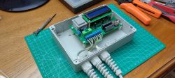 Two-channel DIY timer in a gray case with an LCD display, placed on a green cutting mat on a desk with tools.