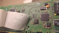 Płytka PCB wzmacniacza BMW z brakującym elementem SMD niedaleko układu scalonego, widoczny fragment osłony ochronnej.