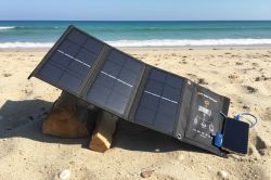 Foldable solar panel on beach, propped with wood, connected to a device via USB