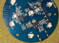 Round blue PCB with LEDs, ICs, and a serpentine wireless antenna on green surface