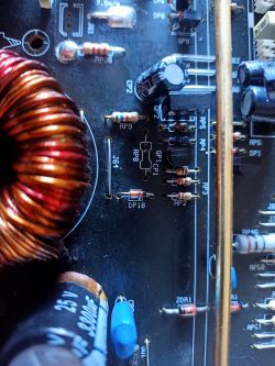 Zbliżenie na płytkę drukowaną wzmacniacza z widocznymi elementami elektronicznymi, w tym cewką i rezystorami.