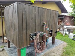 Wooden structure in a garden with attached water hoses and valves.