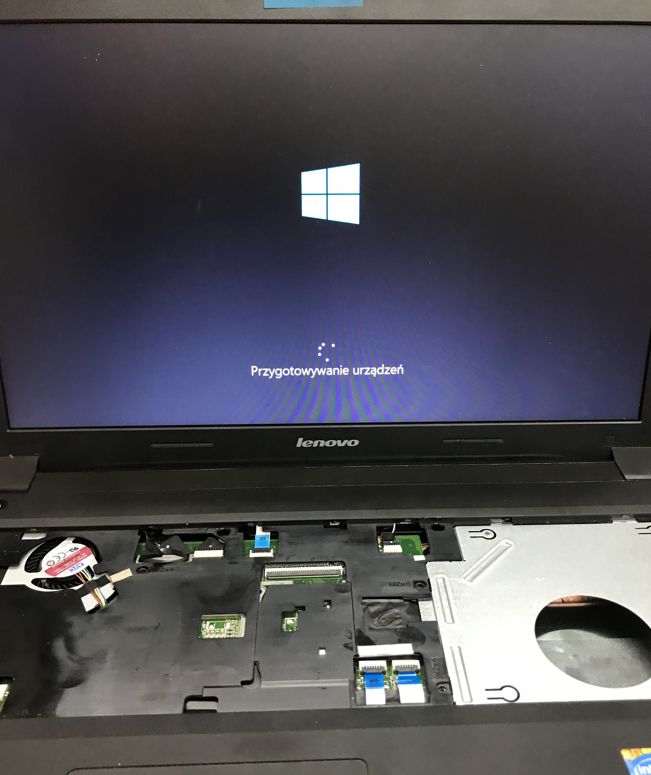 Lenovo laptop with partially opened interior; Windows logo on screen with “Przygotowywanie urządzeń” text.