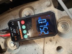 Cyfrowy multimetr na metalowej powierzchni, wyświetla 0,752 V i ma podłączone przewody