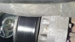 Alternator Mitsubishi z zamontowanym sprzęgłem i widoczną rolką oraz fragmentem napędu w silniku samochodu.