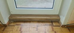 Drewniany parapet zrobiony z deski pod oknem PVC, prowizorycznie zamontowany.