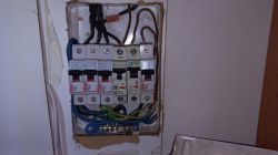 Widok rozdzielnicy elektrycznej z zabezpieczeniami i kablami w środku.