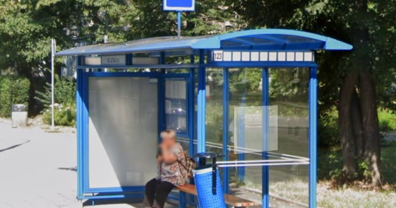 Niebieska wiata przystankowa z numerem 123; na ławce siedzi rozmyta osoba, w tle drzewa.