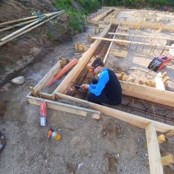A boy wearing safety glasses welds rebar at a building site foundation.