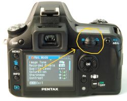 Zbliżenie tylnego panelu aparatu Pentax K100D Super z zaznaczonym uszkodzonym pokrętłem
