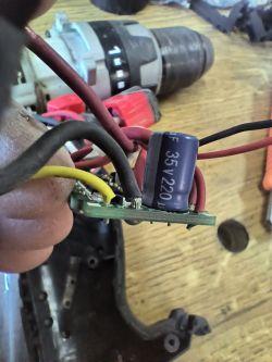 Zbliżenie na płytkę sterownika z zamontowanymi kablami i kondensatorem elektrolitycznym, na tle części wkrętarki.