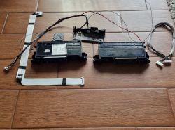 Zdemontowane moduły elektroniczne, wiązki i głośniki z telewizora Sony KDL 65W857C leżące na brązowych płytkach.