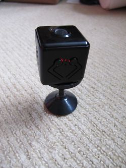 Mini Spy Camera on Magnetic Stand Small black cube-shaped spy camera on a round magnetic stand, placed on a light-colored carpet.
