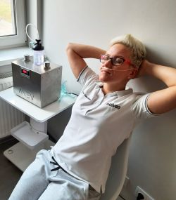 Blonde woman sitting on a chair with nasal cannulas, connected to a device resembling a hydrogen generator.