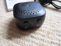 Portable Black Electronic Speaker Small black electronic speaker with two buttons, lying on a beige carpet.
