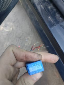 Ręka trzyma niebieski przekaźnik Nissan z numerem 25230 9F920, w tle wystają przewody.
