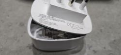 Close-up of a white plug adapter in a white container, with a label and CE markings visible.