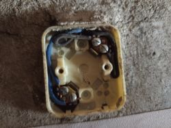 Odsłonięte gniazdko elektryczne w ścianie, bez osłony, z widocznymi przewodami i śrubami.