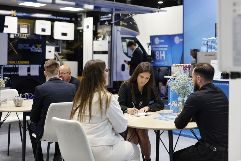Spotkanie biznesowe przy stoliku na stoisku targowym z urządzeniami do magazynowania energii w tle