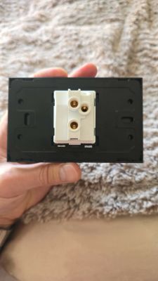 Tył gniazda elektrycznego w czarnej ramce, z białym modułem i trzema mosiężnymi zaciskami