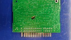 Zielona płytka PCB z uszkodzonym elementem w centrum i złotymi pinami na dole
