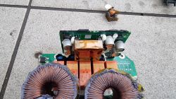 Widok wnętrza uszkodzonej ładowarki/przetwornicy z komponentami elektronicznymi i elementami cewkowymi.