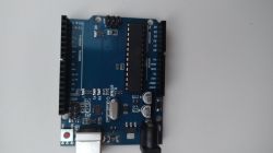 Płytka elektroniczna Arduino UNO leży na białym tle.