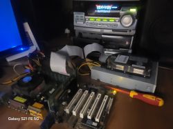 Stara płyta główna komputera z procesorem, kablami IDE, twardym dyskiem i napędem optycznym na biurku obok monitora i wieży stereo.